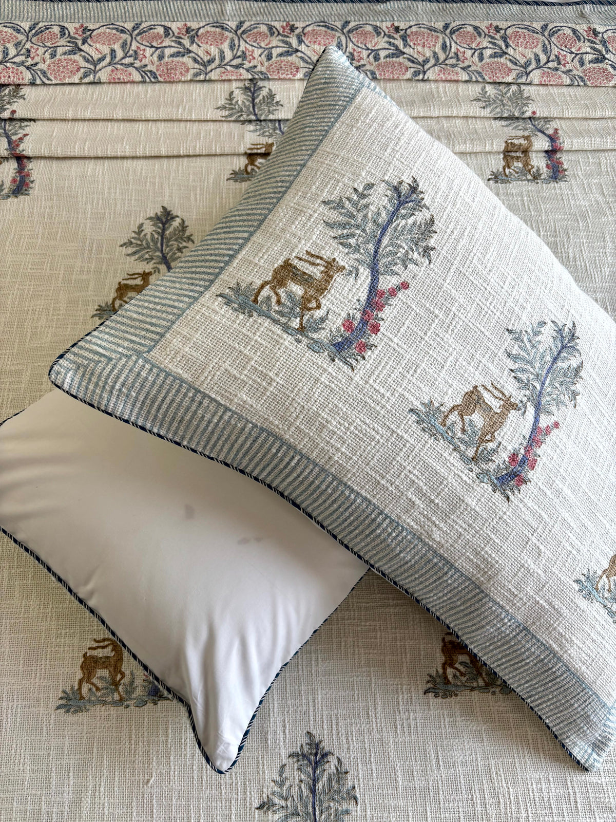 Matching hand block printed pillow covers featuring woodland deer and flowering tree motifs from the Mrigvana Reverie bedcover set.
