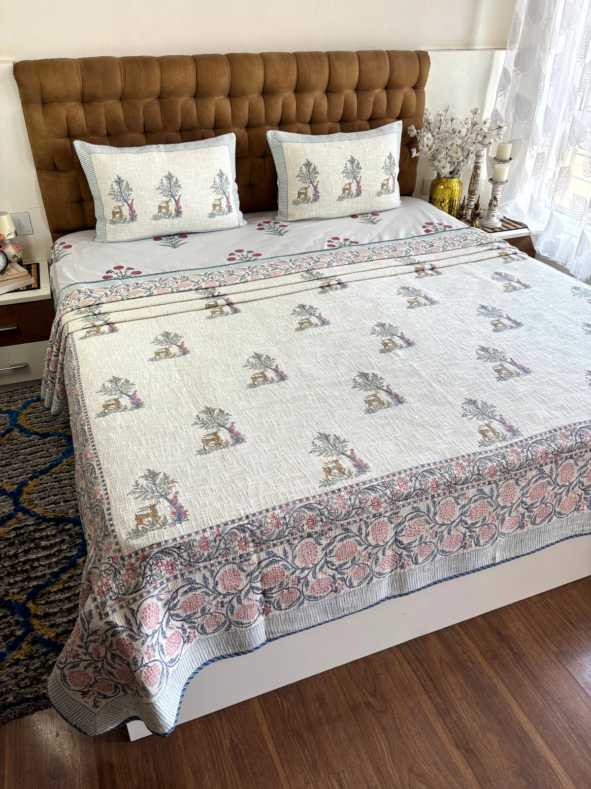 Mrigvana Reverie ivory jute cotton king size bedcover featuring hand block printed deer, flowering trees, and matching pillow covers.
