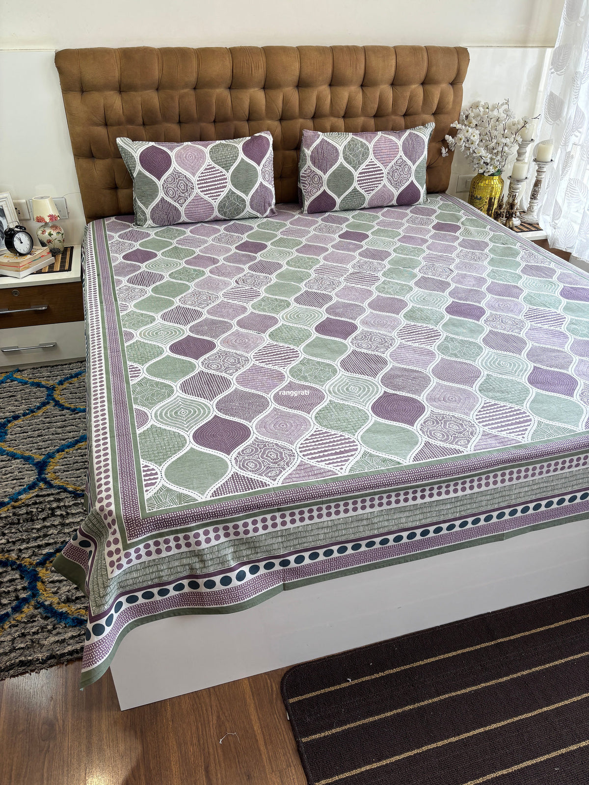 Angled view of the plum and sage green ogee-print bedsheet showing the dotted and striped border
